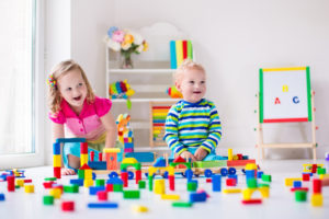 Kids play at day care. Two toddler children build tower of colorful wooden blocks. Child playing with toy train. Educational toys for preschool and kindergarten.